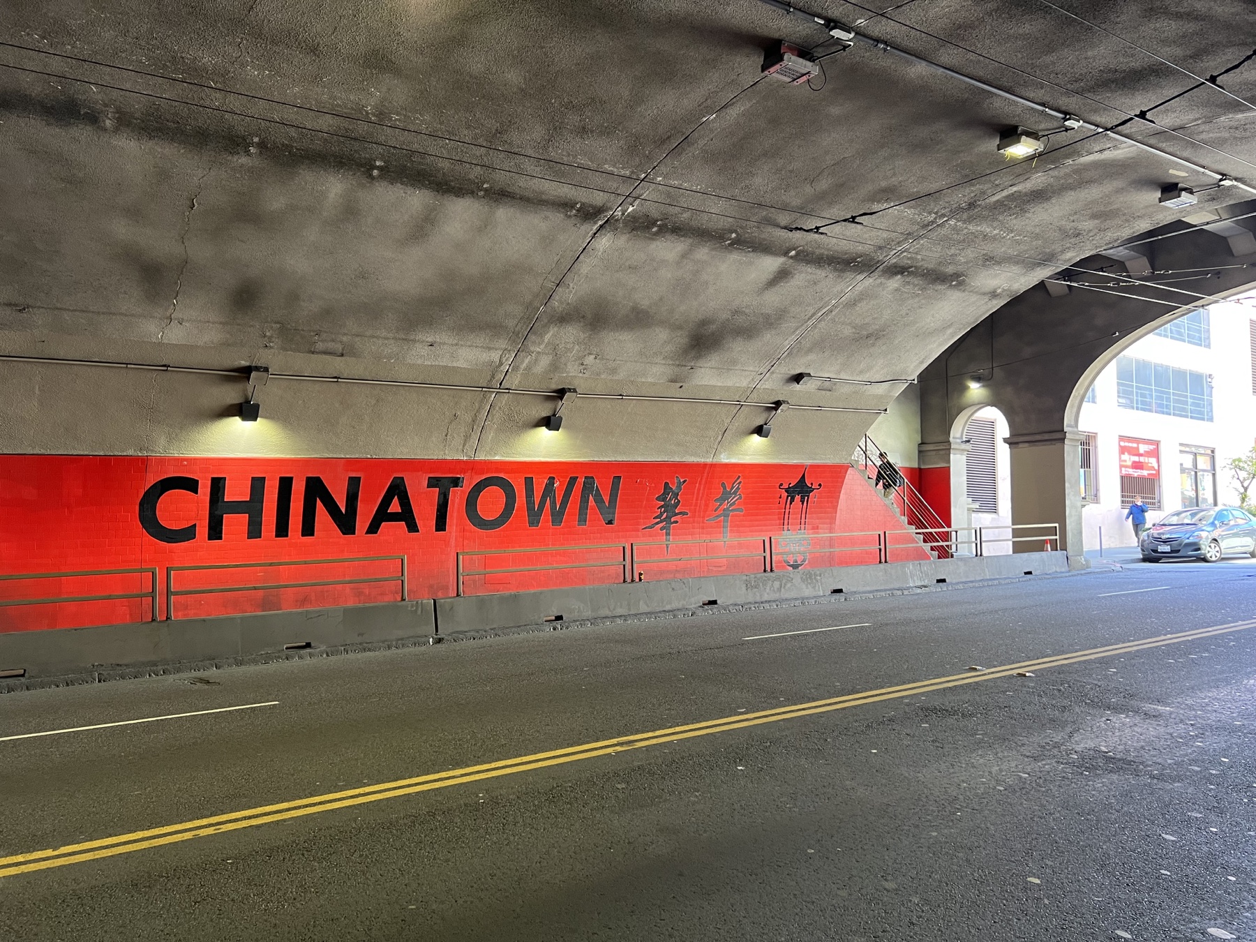 A red Chinatown sign under a concrete overpass in San Francisco.